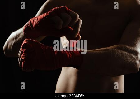 Gros plan sur les mains d'un jeune boxeur qui serpente les bandages rouges avant un match, un combat ou une formation. Banque D'Images