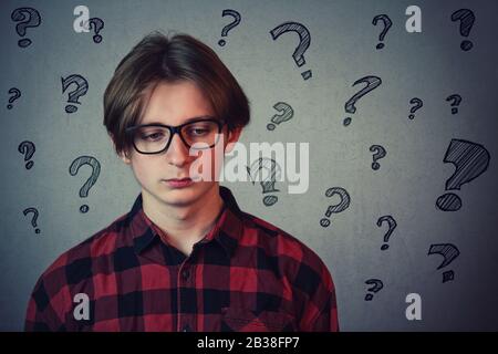 Un adolescent triste et déçu, portant une chemise rouge et des lunettes, regardant vers le bas l'isolement décontent sur fond de mur gris. La personne contrariée a beaucoup de qu Banque D'Images