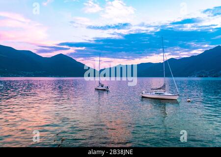 Lac de Locarno avec des bateaux à voile et des montagnes au coucher du soleil Banque D'Images