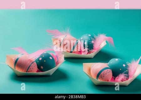 Les œufs colorés décorés de plumes dans des plats de bambou ressemblent à des bateaux sur fond néo-menthe et rose. Concept de Pâques, zéro déchet, écologie Banque D'Images