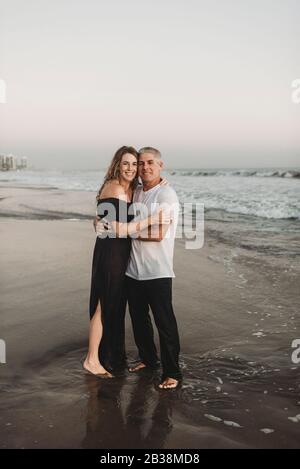 Portrait tranditionnel d'un couple marié debout dans l'océan au coucher du soleil Banque D'Images