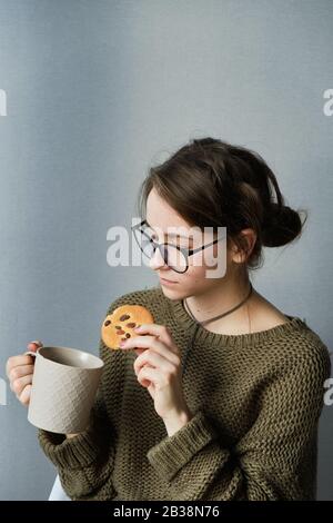 jeune fille à poil brun en verres boire du thé avec des gâteaux seuls Banque D'Images