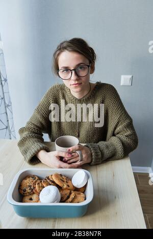 une jeune fille à poil brun du millénaire boit du thé avec des gâteaux Banque D'Images