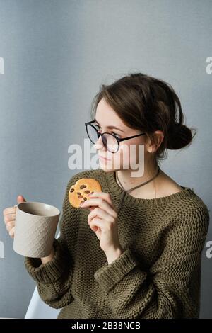 jeune fille à poil brun en verres boire du thé avec des gâteaux seuls Banque D'Images