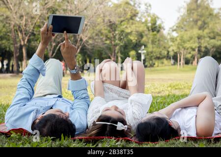 La famille asiatique utilise la tablette sur le tapis. Les filles apprennent à partir d'une tablette que les parents enseignent. Les parents et les enfants jouent à la tablette Banque D'Images