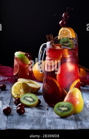 La sangria boit dans un verre et un décanteur avec de la glace et des fruits sur un fond sombre Banque D'Images