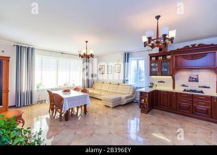 Grande salle lumineuse Sunny dans la maison. Au centre de la chambre se trouve une table avec une nappe blanche et quatre chaises en osier. Canapé en cuir blanc. Vintage Banque D'Images