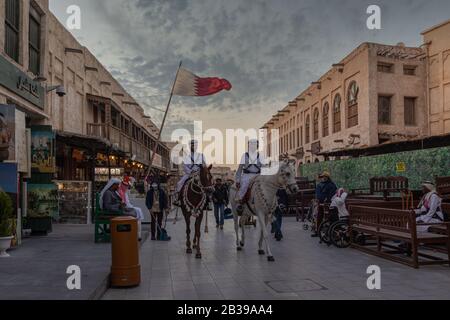 Souk Waqif Doha, Qatar, vue de la rue principale avec des chevaux de police traditionnels et drapeau qatari en arrière-plan Banque D'Images