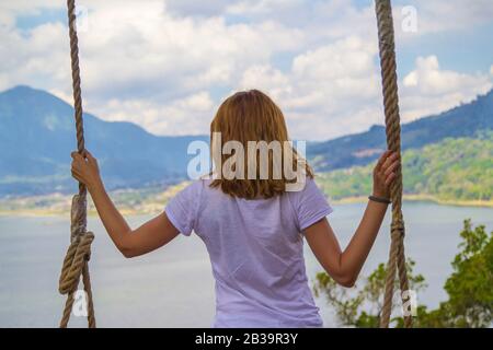 Jeune fille balançant surplombant un lac et des montagnes dans la nature. Banque D'Images