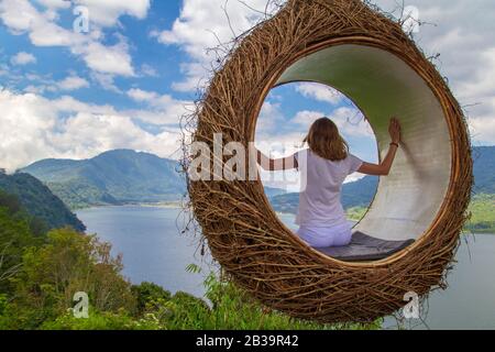 Une jeune fille balançant sur une balançoire sous la forme d'un nid surplombant le lac et les montagnes dans la nature. Banque D'Images
