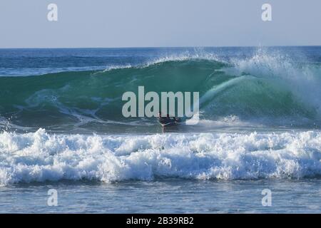 Le surfeur du Bodyboard fait une vague au coucher du soleil. Banque D'Images