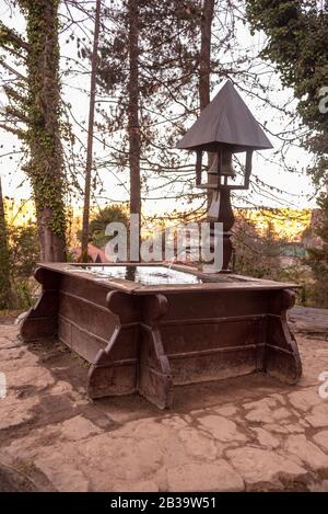 Une fontaine en bois avec un clocher, entourée d'une petite bosquet Banque D'Images