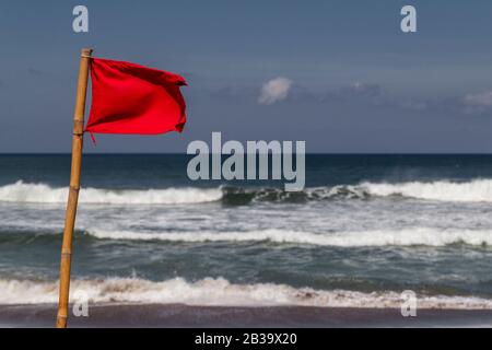 Drapeau rouge qui flotte dans le vent sur la plage par temps orageux. Banque D'Images