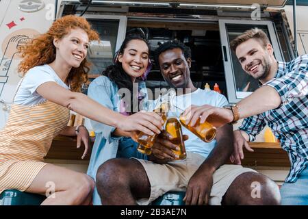 joyeux amis multiculturels qui s'y penchent avec des bouteilles de bière près d'un camion de restauration Banque D'Images