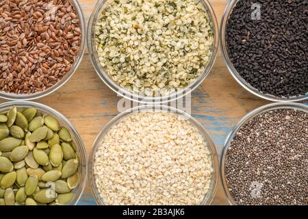 collection de graines saines (chia, coeurs de chanvre, lin brun, citrouille, cumin noir, sésame blanc) - vue de dessus de petits bols en verre contre le bois de grunge Banque D'Images