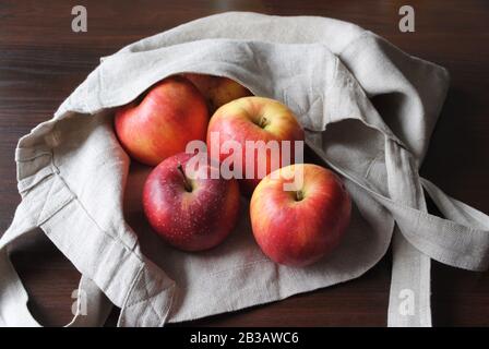 Vue sur le groupe de pommes rouges jaunes colorées biologiques naturelles fraîches avec sac de couleur neutre en lin sur table en contreplaqué sombre, en lumière naturelle Banque D'Images