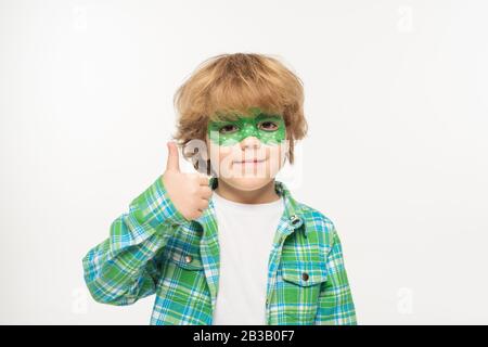 jeune garçon gaie avec masque gecko peint sur le visage montrant le pouce vers le haut tout en regardant la caméra isolée sur blanc Banque D'Images