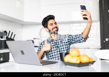 Homme moderne barbu utilisant le téléphone portable et boire du café avec ordinateur portable. Banque D'Images