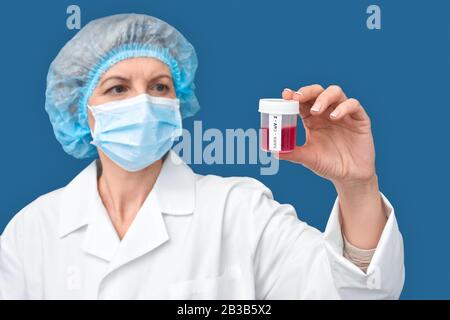 Médecin de femme d'âge moyen contenant un contenant avec test sanguin et vaccin contre le coronavirus Banque D'Images