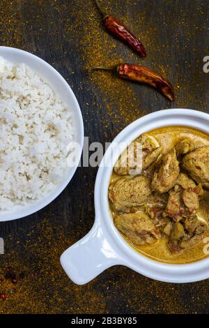 Curry de poulet épicé à l'orange et riz dans des assiettes blanches simples sur fond sombre. Autour de poivre chaud, citron, poudre de curry. Cuisine traditionnelle indienne Banque D'Images