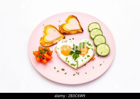 Le petit-déjeuner de la Saint-Valentin est composé d'œufs brouillés, de toasts en forme de coeur au fromage et au jambon. Arrière-plan blanc, vue de dessus. Banque D'Images