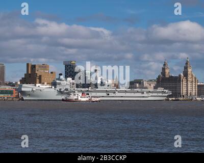 Le ferry Mersey Royal Iris passe devant le porte-avions Prince of Wales de la Royal Navy, amarré au bord de mer historique de Liverpool, classé au patrimoine mondial de l'UNESCO Banque D'Images