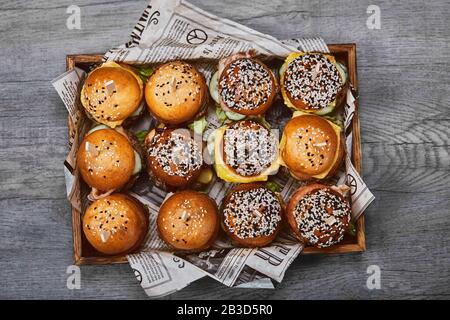 Ensemble De Délicieux cheeseburger dans une boîte en bois sur un fond clair. Une boîte avec différents hamburgers, une offre fixe pour une entreprise Banque D'Images