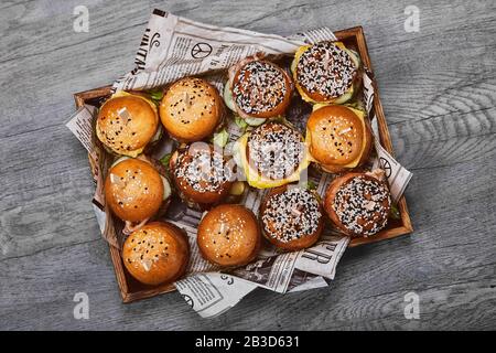 Ensemble De Délicieux cheeseburger dans une boîte en bois sur un fond clair. Une boîte avec différents hamburgers, une offre fixe pour une entreprise Banque D'Images