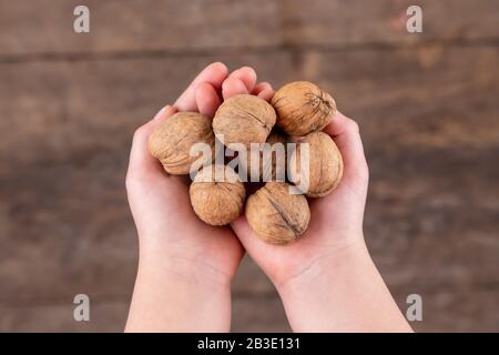 Photo aérienne d'une femme enfant tenant des noix sur une table en bois. Fond en bois. Banque D'Images