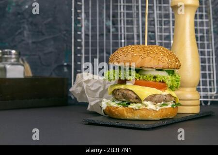 Hamburger gros plan sur un support en graphite, à côté de frites, tomates et poivrons, un support de gril est derrière Banque D'Images