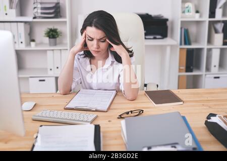 Jeune femme d'affaires perplexe assise au bureau dans un bureau moderne et analysant le contenu du contrat Banque D'Images