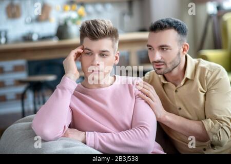 Homme en chemise rose assis sur le canapé se sentant bouleversé et offensé Banque D'Images