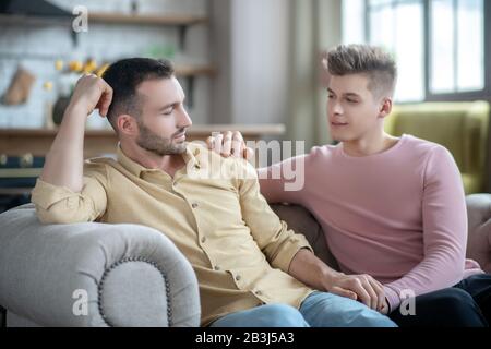 Homme en chemise orange assis sur le canapé ne regarde pas content Banque D'Images