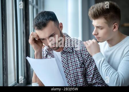 Jeune homme aux cheveux sombres dans une chemise à damier résultats du test de lecture Banque D'Images