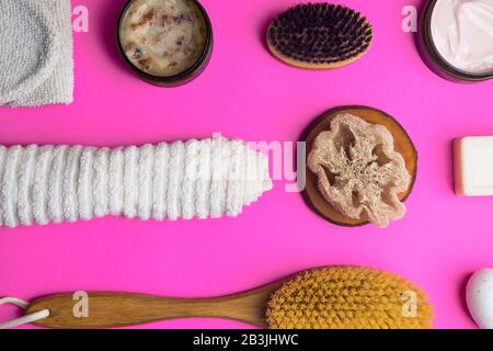 Gommage, lotion, savons, serviette en coton, gant exfoliant pour le soin du corps sur fond rose. Kit spa écologique, plat Banque D'Images
