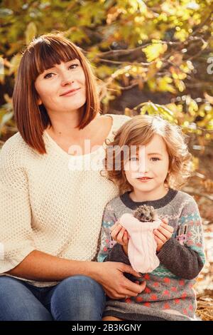 Maman et ses filles sont détenues par un petit hérisson. Peinture d'automne tactile, feuilles d'automne jaunes en arrière-plan Banque D'Images