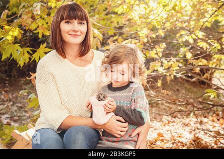 Maman et ses filles sont détenues par un petit hérisson. Peinture d'automne tactile, feuilles d'automne jaunes en arrière-plan Banque D'Images