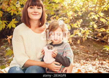 Maman et ses filles sont détenues par un petit hérisson. Peinture d'automne tactile, feuilles d'automne jaunes en arrière-plan Banque D'Images