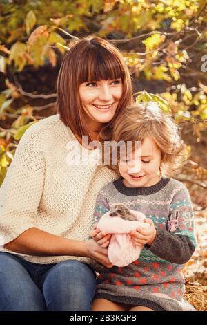 Maman et ses filles sont détenues par un petit hérisson. Peinture d'automne tactile, feuilles d'automne jaunes en arrière-plan Banque D'Images