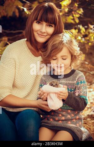 Maman et ses filles sont détenues par un petit hérisson. Peinture d'automne tactile, feuilles d'automne jaunes en arrière-plan Banque D'Images