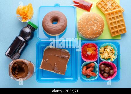 Boîte à déjeuner avec nourriture malsaine sur fond bleu, vue de dessus Banque D'Images