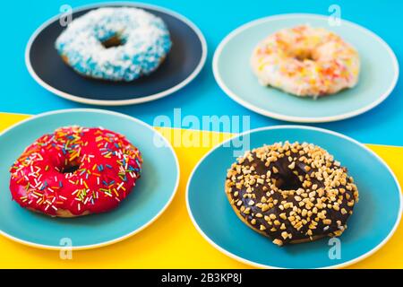 4 beignets frais appétissant sur la plaque sur fond jaune et bleu. Concept de la nourriture douce. Banque D'Images