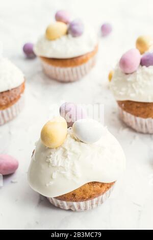Cupcakes de Pâques glacés décorés de mini œufs au chocolat sur fond de marbre blanc. Joyeuses Vacances De Pâques. Banque D'Images