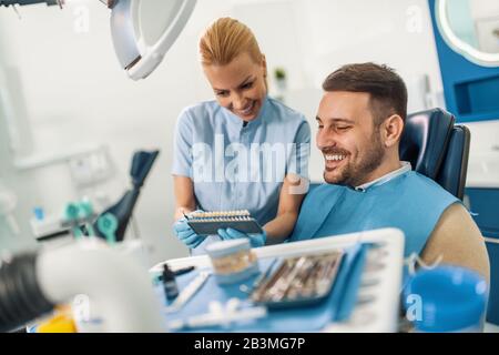 Le médecin compare les dents du patient avec le tableau de blanchiment dentaire.gros plan du patient avec un beau sourire chez le dentiste. Banque D'Images