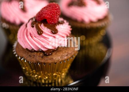 Des cupcakes au chocolat gourmets, arrosés de ganache au chocolat et recouverts d'une framboise fraîche. Banque D'Images