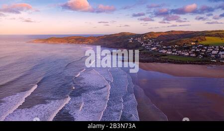 Vue aérienne de la ville de Woolacombe et de sa plage à l'aube, vagues se brisant sur une plage, la pointe de Morte point baignée de soleil et de brumeux avec Banque D'Images