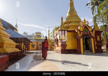 Un moine dans des robes de salon tenant un personnel et un bol en acier d'alms debout dans le domaine d'un temple, Sittwe, Rakhine, Myanmar (Birmanie), Asie Banque D'Images