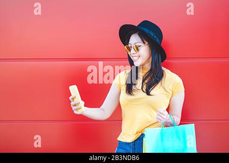 Une fille de mode asiatique faisant des achats dans le centre commercial en utilisant un smartphone mobile - Une Femme chinoise Heureuse ayant du plaisir à acheter de nouveaux vêtements en vacances Banque D'Images