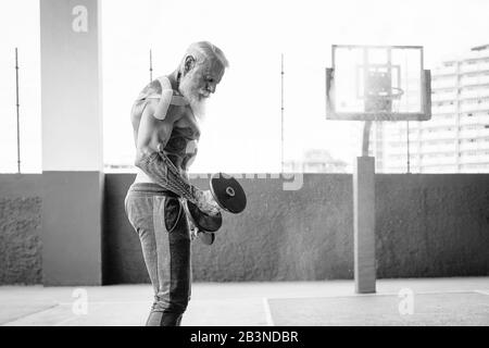 Homme de fitness senior faisant des biceps exercices de curl à l'intérieur de la vieille salle de gym - Fit mature entraînement masculin avec des haltères dans le centre de club de bien-être Banque D'Images