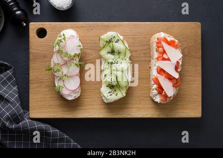 Trois sandwichs différents sur pain grillé avec légumes frais, radis, tomates, concombres et microgreens sur fond noir. Vue de dessus. Banque D'Images